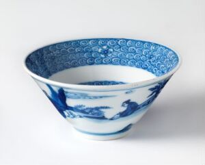  A traditional blue and white porcelain bowl with intricate patterns, featuring a landscape scene on the outside and a decorative rim, placed on a neutral surface.