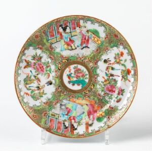  A highly ornate porcelain plate with scalloped edges featuring colorful scenes with figures and floral patterns in red, green, blue, and yellow, displayed upright on a clear stand.