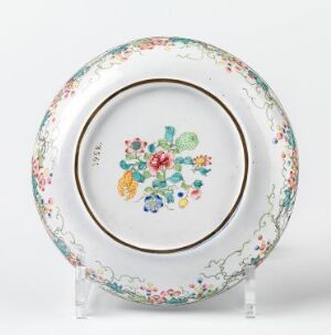 alt-text: A decorative porcelain plate with a gold-rimmed edge and a central hand-painted bouquet of flowers in blues, reds, pinks, and yellows, surrounded by an intricate border of interlacing foliage patterns in various colors.