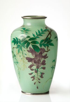  A tall, mint green vase with graceful curves and a narrow neck, adorned with naturalistic dark green foliage and purplish-brown flowers, against a plain background.