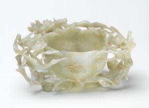  A carved, creamy white bracelet or circular band with intricate openwork of flowers and leaves carved out of a semi-translucent material, displaying delicate craftsmanship and a pearly sheen.