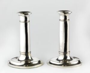  Two polished silver candlesticks with tapered columns and broad, circular bases displayed against a light gray background.