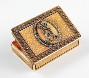  A small, rectangular trinket box with a hinged lid displays a textured, creamy-beige surface with a central golden medallion featuring an embossed crest. The lid is framed by a border of golden beads, and the box exudes a sense of antiquity and luxury.