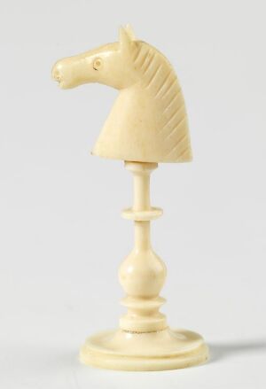  A delicately carved pale cream knight chess piece, featuring intricate details, stands on a slender column with a round base against a light gray background.