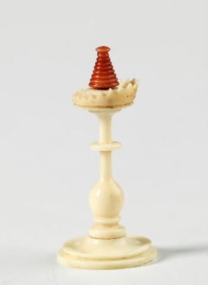  An ivory chess bishop with a broken top, upon which sits a small, detailed red conical object with ridges, all against a plain light background.