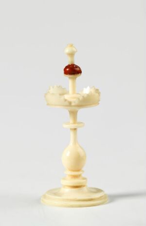  A cream-colored ivory-like chess king with a detailed crown and a small red jewel beneath the cross at the top, set against a plain light background.