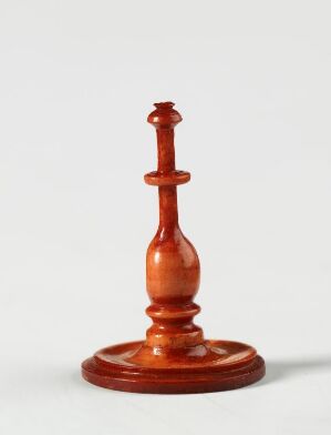  A wooden chess king piece with a red-brown hue, standing against a light gray background, detailed with polished curves and a small cross on the top.