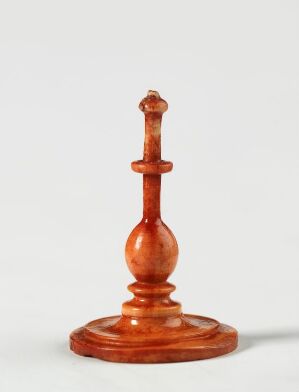  A polished reddish-brown wooden decorative object with a candlestick or a king chess piece look, featuring a spherical midsection and a crowned finial top, on a plain off-white background. Artist and title are unknown.