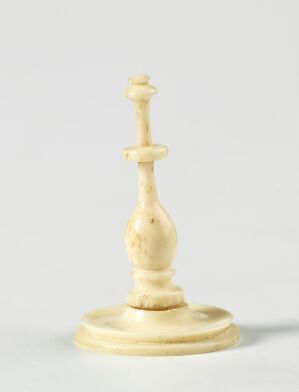  An ivory-colored chess king piece against a light grey background. The piece has a detailed crown with a cross-shaped finial and is standing in a soft, diffuse light, casting a slight shadow to the right.