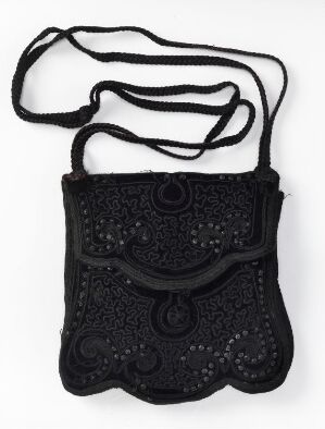  A small, intricately designed lace-like black purse with a plaited strap and a decorative flap secured by a loop over a central button, displayed against a neutral background.