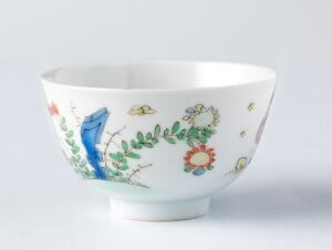  A white porcelain bowl with a flared rim featuring a vibrant illustrative design including a blue bird, colorful flowers, and greenery on its exterior.