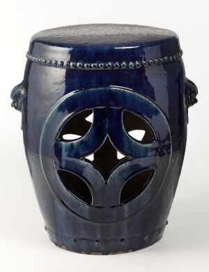  A cobalt blue ceramic garden stool with a shiny glaze. It has an openwork quatrefoil design in the middle, looped handles below the top rim, and bands of slightly lighter blue around the top and bottom edges.