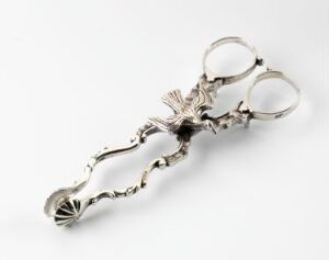  Silver sugar tongs designed by Jens Kahrs with intricate floral and leaf profiles and cast decorations, reflecting light off its shiny, polished surface against a plain light background.