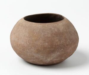  A textured spherical clay bowl with a crosshatched pattern on the exterior in light tan and muted terracotta colors, featuring a dark-colored interior, set against a light neutral background.