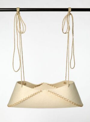  A felt cradle by Søren Ulrik Petersen, suspended by cream-colored linen cords from a black bar. The cradle is made of light tan felt with decorative stitching along the edges, hinting at a comfortable interior.