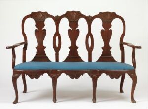  An antique wooden settee with a teal-blue cushioned seat, featuring a highly decorative and symmetrical fiddle-back design, standing against a plain background.