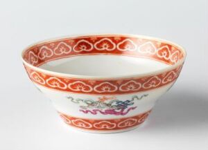 
 A delicately hand-painted Chinese porcelain bowl with an orange-red decorative border and multicolored floral designs on a white background, angled to show the interior and exterior patterns.