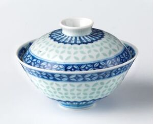  A porcelain rice bowl with a lid on a white background, showcasing intricate white and blue patterns with traditional East Asian design elements.