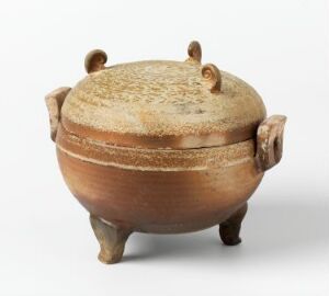  A terracotta ceramic vessel titled "Ding," a religious object with three legs, two loop handles, and a textured lid. The body features a horizontal band with parallel line decorations and variations in reddish-brown coloring. Artist name is Ukjent.