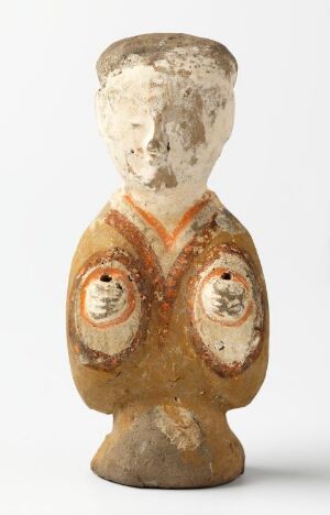  Aged, possibly ceramic bust of a stylized human figure with a simple facial representation and a hand-painted vest featuring circular motifs, set against a neutral background. The figure displays signs of wear, with chips and faded areas revealing a white undercoat or raw material.