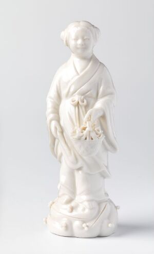  A porcelain figurine titled "Lan Caihe" by an unknown artist, depicting a standing androgynous figure in flowing robes with a gentle expression, holding a flower basket. The monochromatic piece is off-white with a glossy finish, and the figure stands on a base resembling stylized clouds.