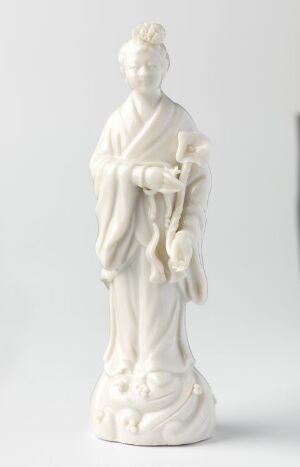  A white glazed porcelain figurine of He Xiangu, by an unknown artist, depicting a graceful female figure with flowing robes and serene expression, set against a neutral background.