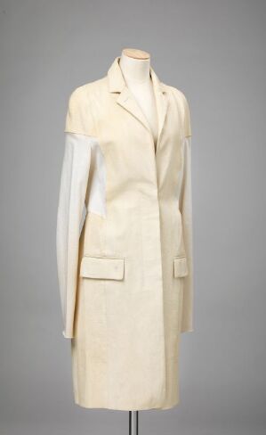  An elegant creamy white, full-length coat designed by Helmut Lang is displayed on a mannequin against a grey background. The coat features a structured collar, machine-sewn leather details, and practical large patch pockets, with a sophisticated, minimalistic design.