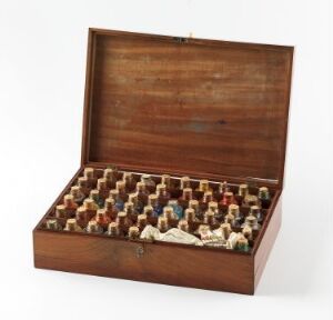  An open, vintage wooden box with rows of small, variously colored figurines arranged neatly inside, displaying a collection of characters or symbols.