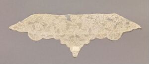  A delicate antique lace fabric with intricate floral patterns and a scalloped edge, displayed against a neutral gray background.