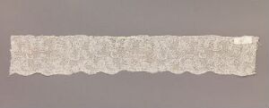  A detailed image of a delicate, creamy white strip of lace with scalloped edges, placed on a neutral gray background. The lace displays a complex, intricate pattern, indicative of fine craftsmanship.