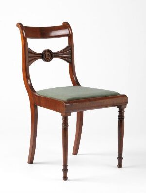  A traditional wooden chair with a mahogany finish and a sage fabric seat against a white background. It features a curved backrest with a carved rosette and graceful open arcs.