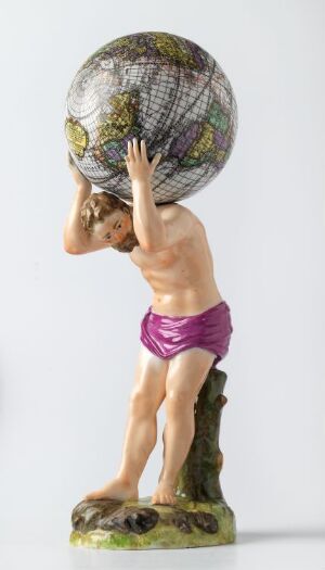  A glazed porcelain figure by Den kgl. Porcelainsfabrik titled "Altas bærer jordkloden," depicting the mythological figure Atlas in flesh tones with defined muscles, crouching while carrying a globe with detailed latitude and longitude lines on his back. He wears a bright purple cloth around his waist, standing on a base that resembles natural earth and grass.