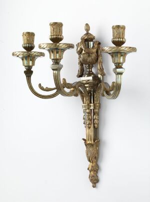  An antique gold-colored wall candelabra with three arms and ornate carvings featuring naturalistic designs and classical elements.