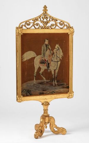  An antique fire screen stand with a golden ornate frame showcasing monochromatic artwork of a historical figure riding a horse in profile, set against a warm reddish-brown background.