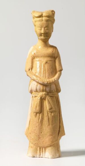  A vertically-oriented image of an intricately carved ivory-colored figurine depicting a person with historical attire and an upright hairstyle, clasping hands at the waist, against a plain light gray background. The figure conveys a sense of antiquity and serenity.