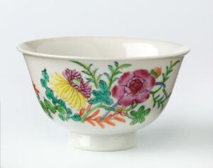  A porcelain bowl with a footed base and flared rim, decorated with a vibrant, hand-painted floral pattern featuring a large pink rose, yellow and purplish-pink flowers, and varied green foliage on a creamy white background.