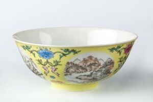  A shallow, wide-rimmed bowl with a creamy yellow exterior, decorated with vibrant floral patterns and a monochromatic mountain landscape, set against a white background. Artist name and title unknown.