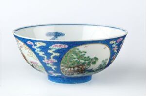  A richly colored, cobalt blue porcelain bowl with ornate floral patterns and a landscape scene in an oval panel. The bowl is set against a plain white background, highlighting its vibrant and traditional design.