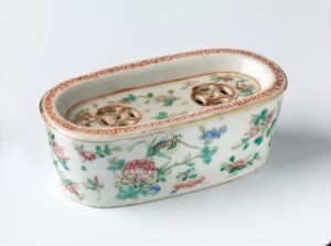  An oval-shaped antique ceramic dish with a white background and a delicate pattern of hand-painted flowers in soft pinks, blues, and greens with a terracotta-edged rim.