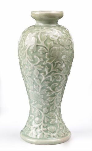  An elegant celadon green ceramic vase with a detailed surface pattern of raised, carved scrolling botanical motifs. The vase is elongated with a flared top, a straight neck, and a slightly everted lip edge, set against a plain light background.