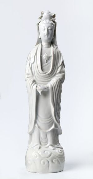  A monochromatic, white sculpture of a serene, robed figure, possibly a deity from East Asian culture, standing on a lotus-decorated base with hands in a symbolic gesture, radiating a sense of grace and inner peace.