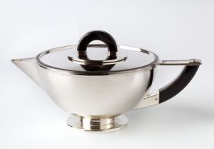  A silver metal teapot with a modern design, featuring a reflective surface, black handle, and knob set against a white background. The artistname and title are not provided.