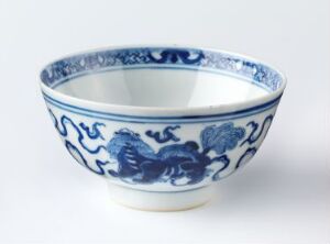  A traditional Chinese porcelain bowl with intricate blue patterns on white background, featuring stylized waves and mythical creatures on the outer surface and a decorative blue band along the rim.