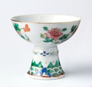  A finely painted porcelain bowl with a flared rim and pedestal base, featuring hand-painted floral designs in pastel pinks, warm oranges, and vivid greens, interspersed with touches of blue, purple, and white, suggestive of a