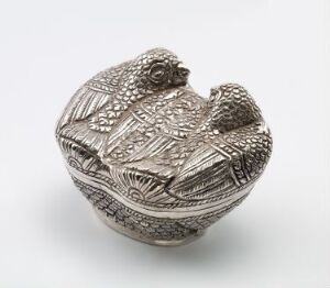  A detailed silver sculpted object of a hen nesting on eggs, showcasing textured patterns and a monochromatic silver color scheme, reflecting soft light and intricate craftsmanship.