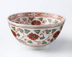  An ornate ceramic bowl on a white background, featuring an off-white base color elegantly decorated with a symmetrical floral pattern in varying shades of green and red.