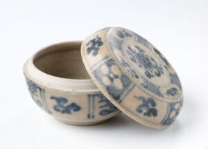  A small, round ceramic trinket box with a lid, adorned with blue floral patterns on a creamy white background, showcasing traditional porcelain design.