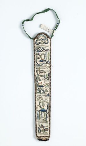  A narrow, vertically oriented embroidered bookmark with a loop at the top for hanging. The bookmark displays intricate designs with a stylized face at the top followed by a series of compartmentalized animal figures in a predominately off-white, blue, and brown color palette on an antique-looking fabric.