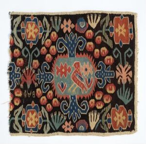  An intricately patterned textile with a black background and a central medallion of blue and red, surrounded by colorful floral and geometric shapes in red, blue, green, and orange. The fabric edges appear slightly frayed. The artist name and title are unknown.