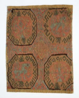  An antique-looking textile featuring a pattern of four large, overlapping sienna medallions with stylized teal animals and ochre geometric floral patterns on a faded terracotta background, connected by small leaf-like motifs.